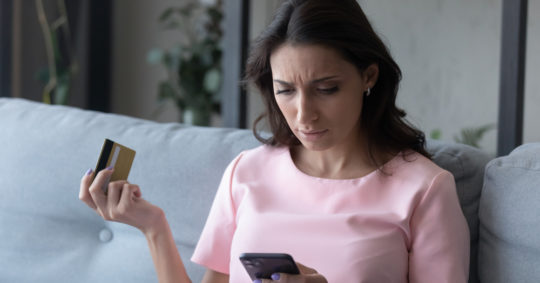 Confused woman holding phone and credit card