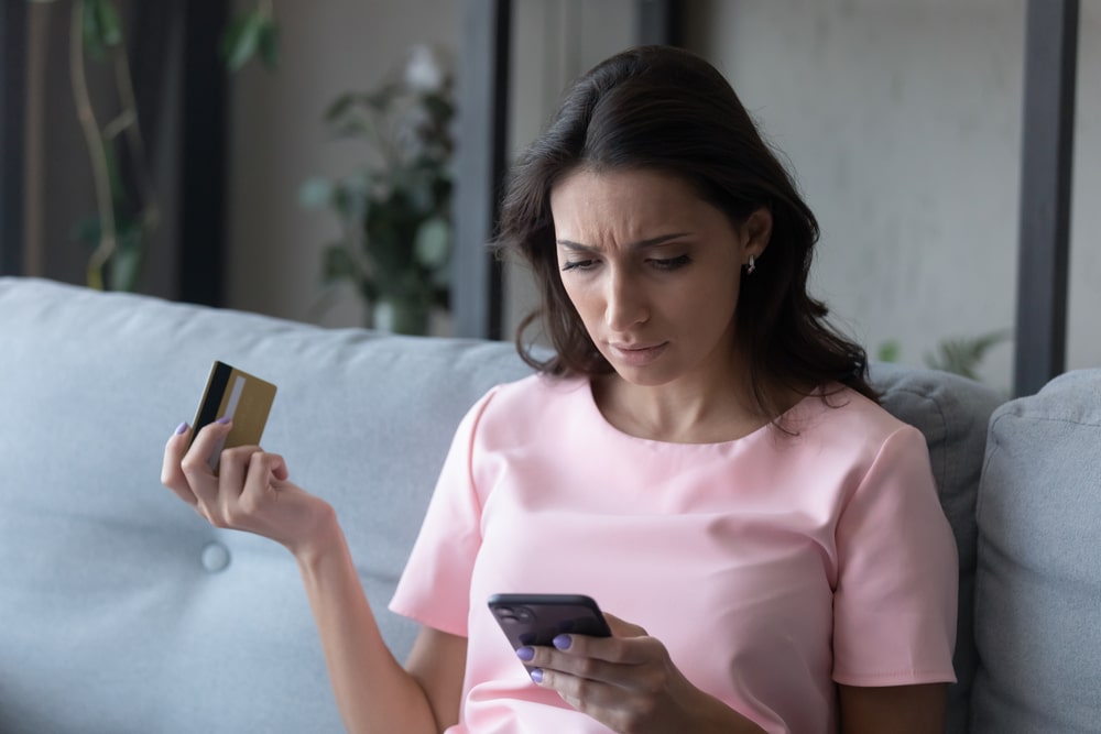 Confused woman holding phone and credit card