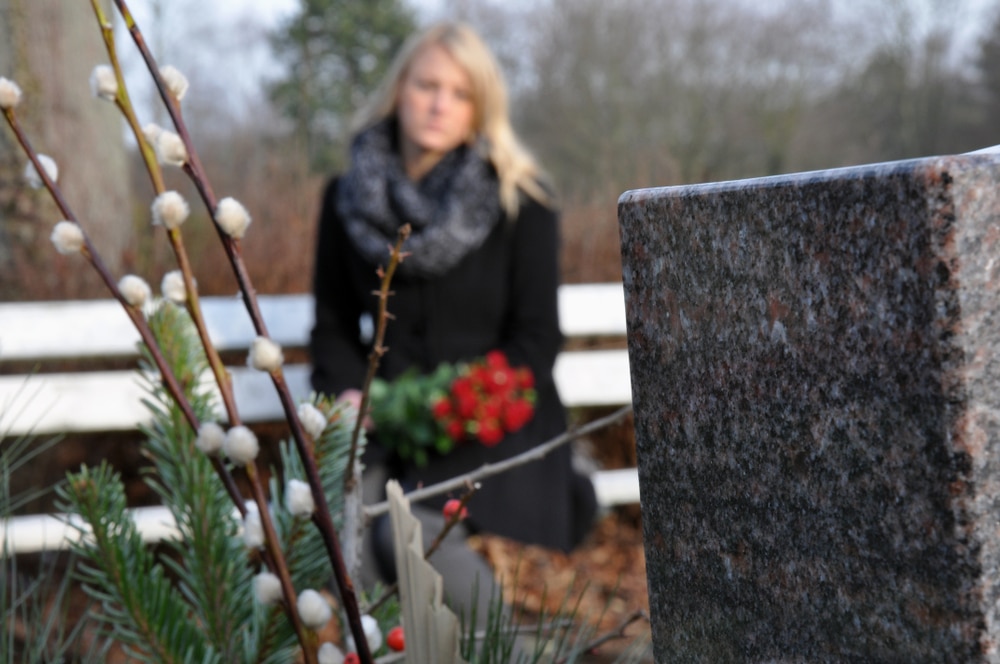 woman sitting in a cemetery looking at a gravestone