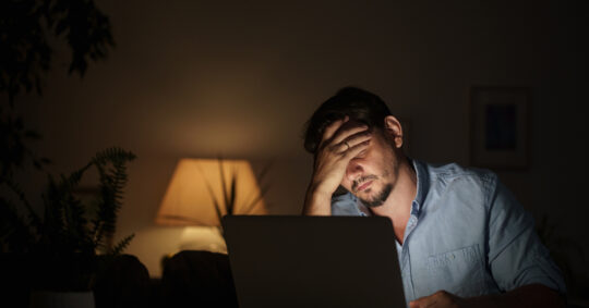 overwhelmed man searches internet with laptop at nighttime inside house