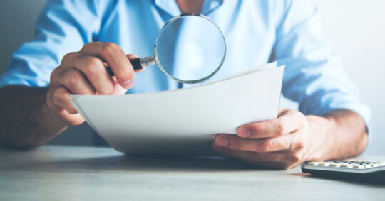 person with magnifier checking paper